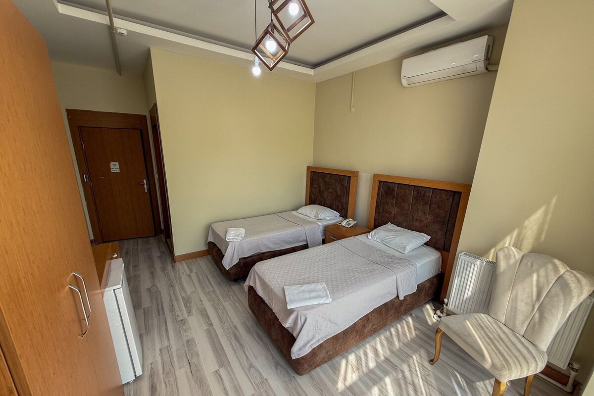 A hotel room with two beds, a chair, a wardrobe, and an air conditioning unit.