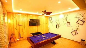 Una mesa de billar en una habitación con paredes de madera, un ventilador de techo y adornos en la pared.