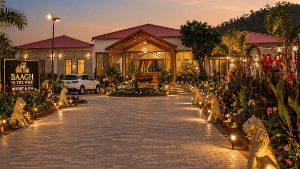 Entrada de un resort con un camino pavimentado, un coche blanco estacionado y un letrero que dice 'BAAGH IN THE WILD RESORT & SPA'.