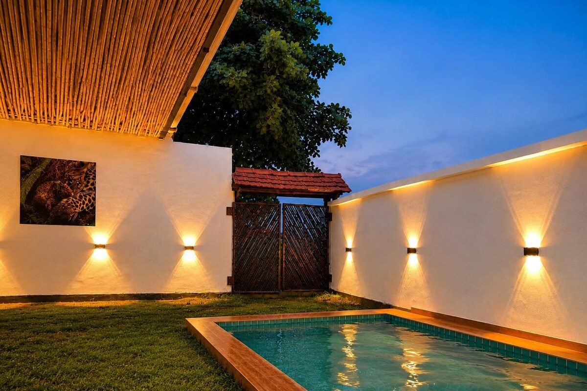 A swimming pool with a wooden deck, surrounded by walls with wall-mounted lights, and a gate in the background.
