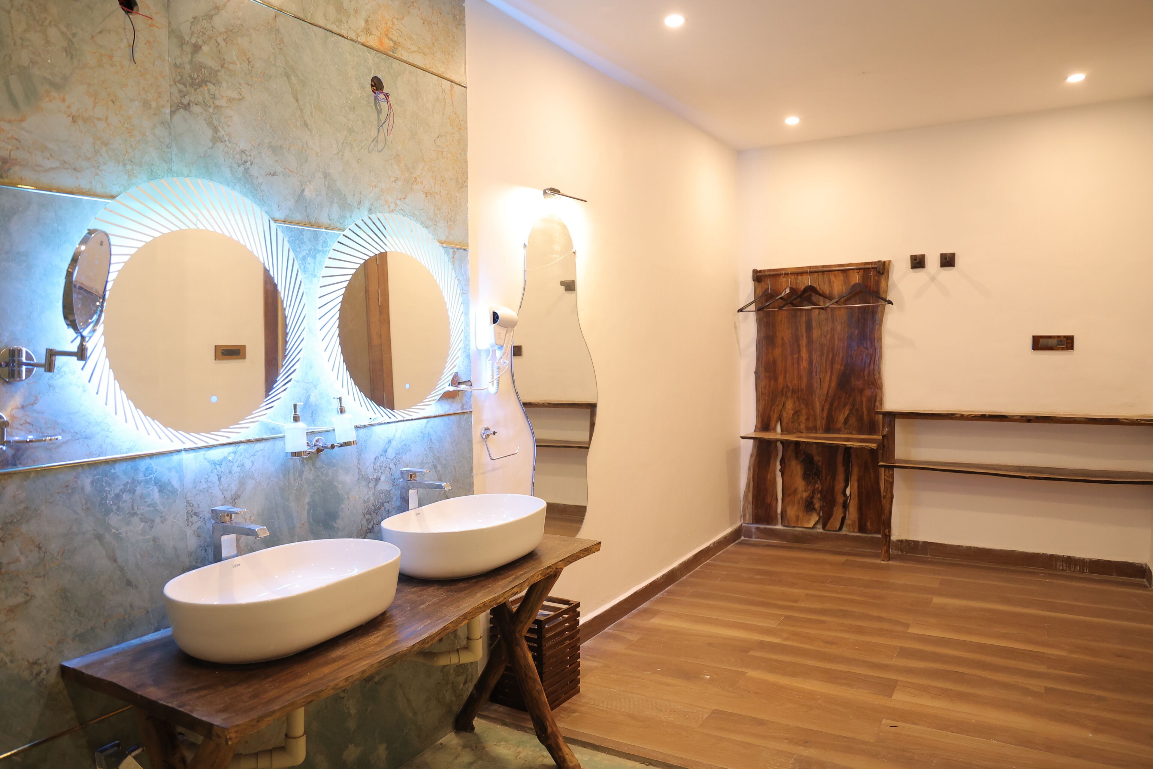 Un baño con dos lavamanos, un mueble de tocador de madera y un espejo grande con luces circulares.