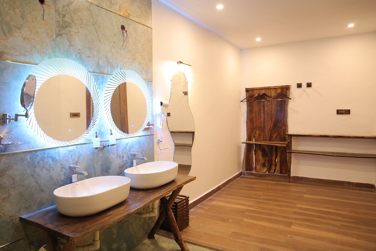 A bathroom with two sinks, a wooden vanity, and a large mirror with circular light fixtures.