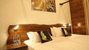 A hotel room with a wooden headboard, a painting of a leopard's face, and two bottles of water on the nightstand.