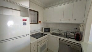 Eine kompakte Küche mit weißen Schränken, einer Mikrowelle, einem Toaster und einem Geschirrspüler.