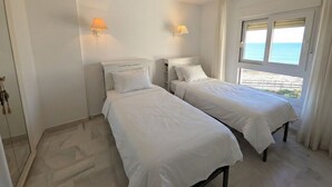 Ein Zimmer mit zwei Betten, einem Fenster mit Meerblick und einer Tür mit Griff.