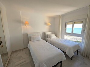 Ein Zimmer mit zwei Betten, einem Fenster mit Meerblick und einer Tür mit Griff.