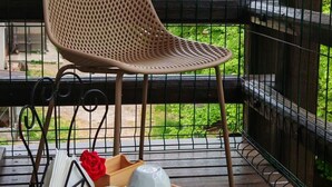 Una silla de mimbre sobre una terraza de madera, con una bandeja de vajilla blanca y una rosa roja.
