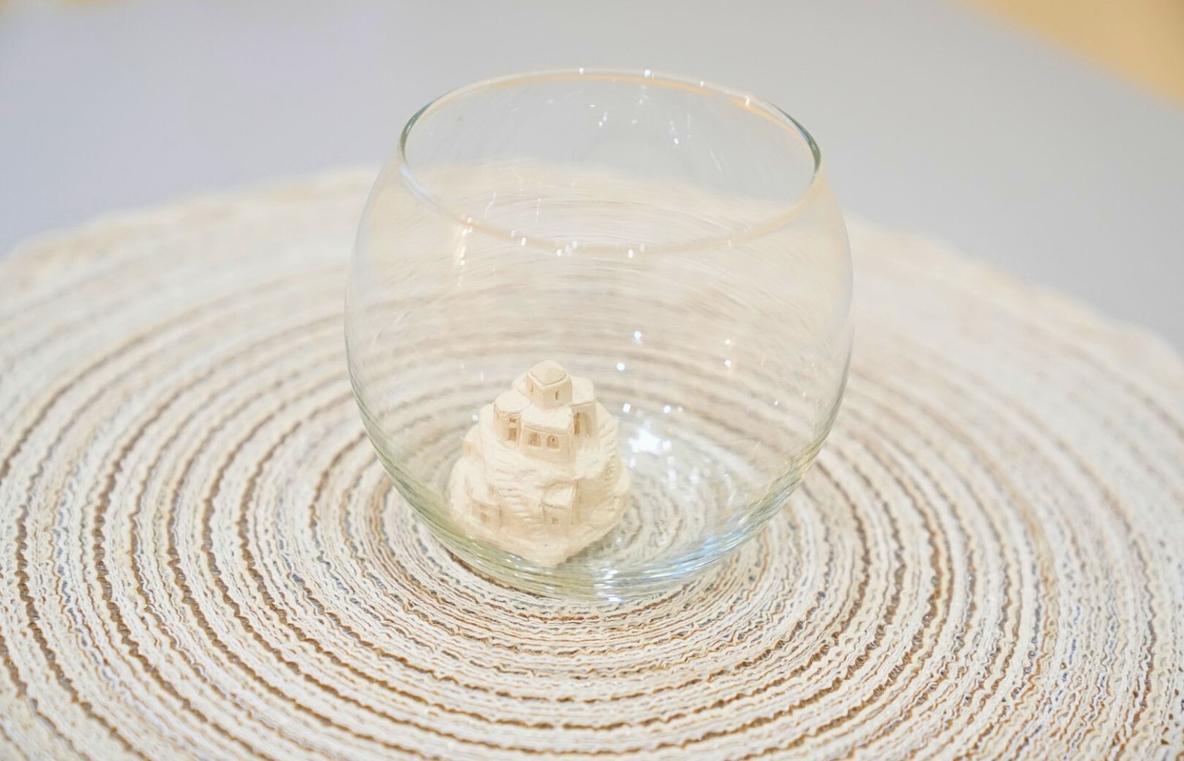 Un cuenco de vidrio transparente con un objeto blanco en su interior, sobre una superficie texturizada.
