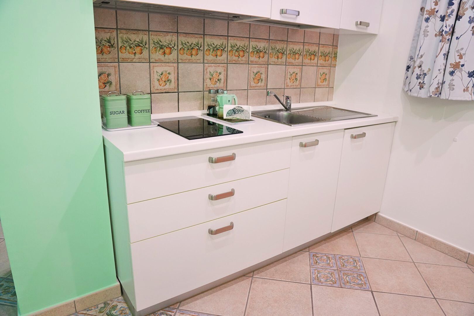 Una cocina con gabinetes blancos, un lavamanos doble y contenedores verdes para guardar, etiquetados 'SUGAR' y 'COFFEE'.