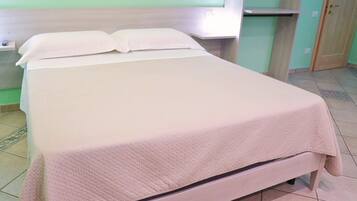 Un lit avec un matelas blanc et une couverture à motifs, une table de chevet et une étagère fixée au mur.