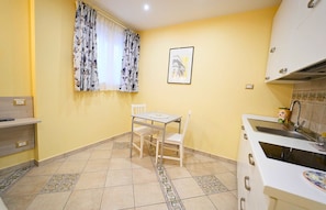 A compact kitchen with a dining table, chairs, a window with floral curtains, and a sink. - Villa Vittoria (Matera)