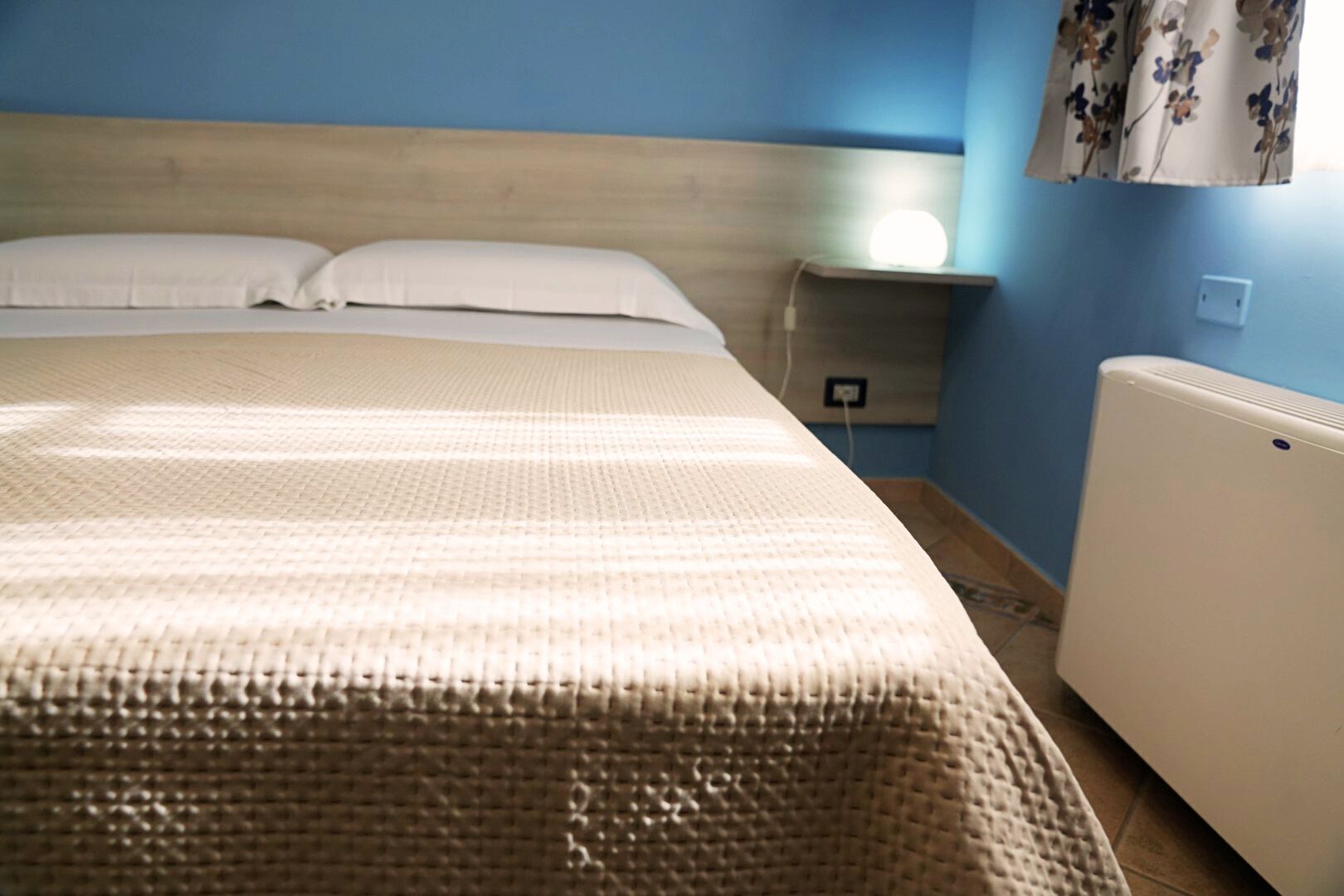 A bed with a textured bedspread, a bedside table with a lamp, and a radiator.