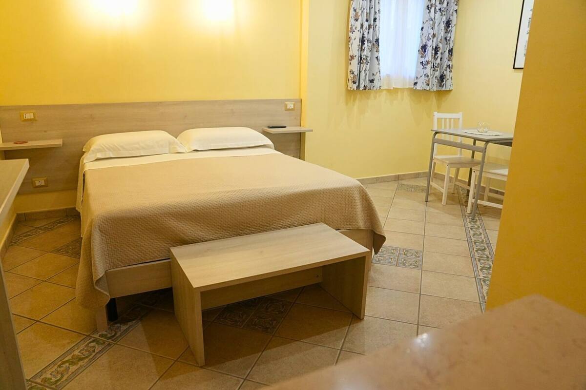 A hotel room with a bed, bedside tables, a bench, a small table, and a chair.