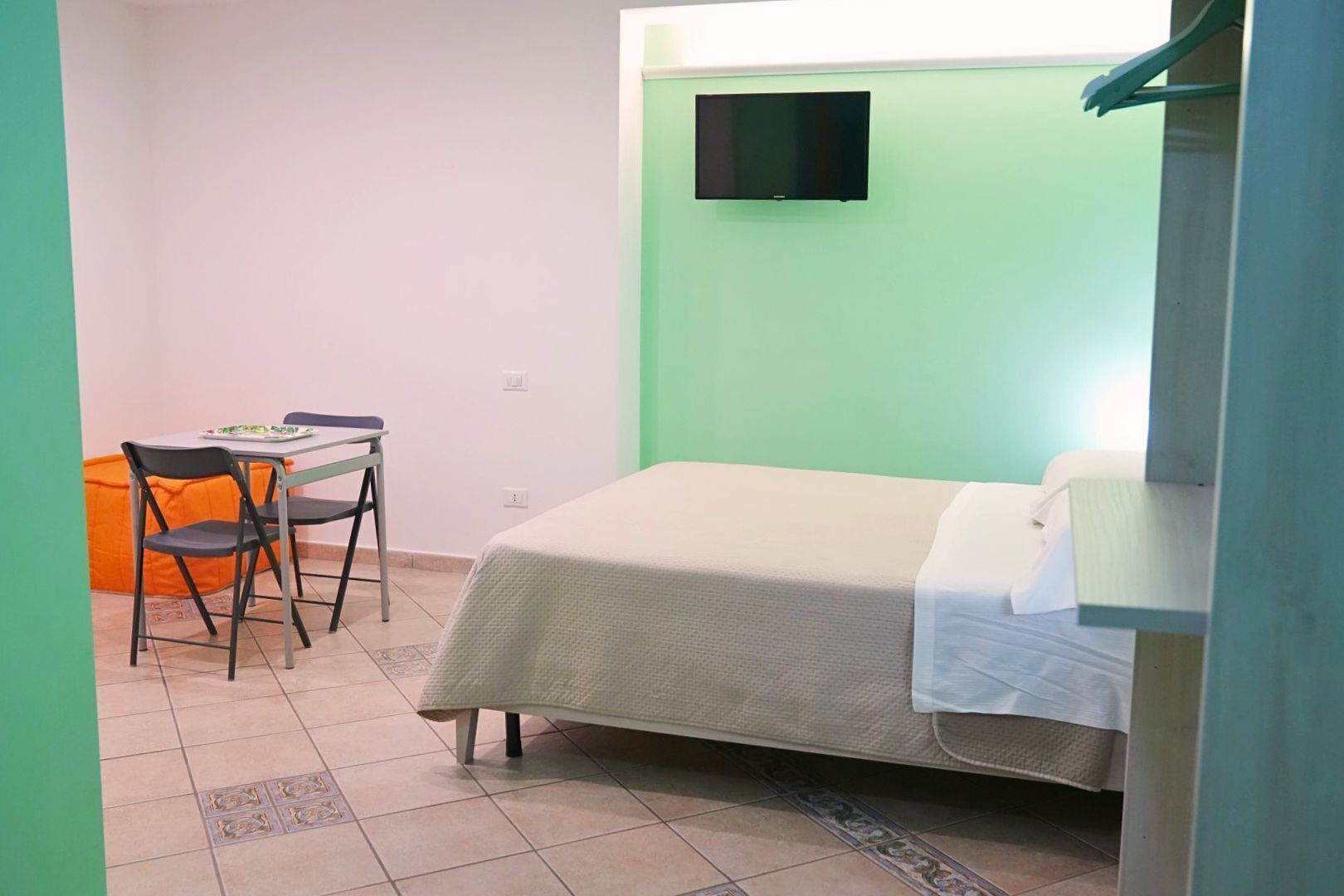 Una habitación con una cama, un escritorio con una silla y un televisor instalado en la pared.