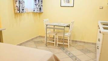 A small room with a table and chairs, a bed, a cabinet, and a window with curtains.