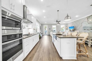 A modern kitchen with white cabinetry, stainless steel appliances, and a central island with bar stools. - Ocean Pearl by Stay on 30a (Inlet Beach)