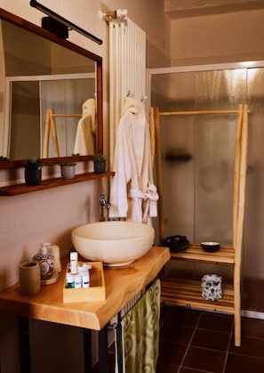 Ein Badezimmer mit einem Holzkosmetikschrank, einem großen weißen Waschbecken, einem Spiegel, einem Handtuchhalter und einer Duschkabine.