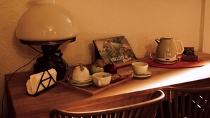 Ein Tisch mit einer Lampe, einem Buch, einer Teekanne, Tassen und einer Tablett mit Speisen.