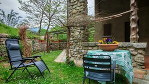 Ein Steinhaus mit Tisch und Stühlen, einem Blumentopf und einem mit Weinreben bewachsenen Spalier.