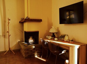 Ein gemütliches Zimmer mit Kamin, einem an der Wand befestigten Fernseher und einem kleinen Tisch mit Stühlen.