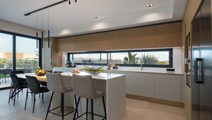 Een moderne keuken met een groot eiland, barstoelen, een eettafel en uitzicht door een groot raam.