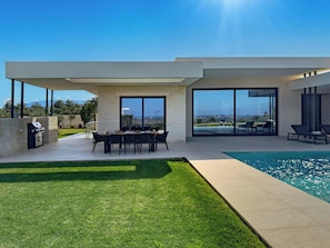 Ein modernes Haus mit Pool, Essbereich und Grillplatz.