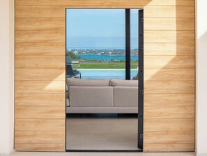 Ein modernes Zimmer mit einer großen Schiebeglasdoor zu einem Pool und Blick auf eine Küstenlandschaft.