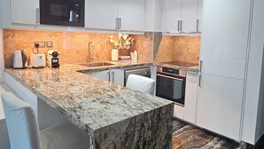 Una cocina moderna con armarios blancos, una isla de granito y un salpicadero de mármol.
