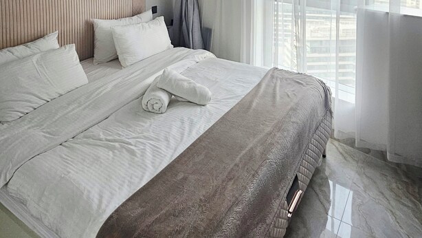 Una habitación de hotel moderna con una cama grande, cabecero, un cuadro en la pared y vistas a la ciudad a través del ventanal.