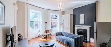A modern living room with a fireplace, a sofa, a dining area with chairs, and a kitchen area with a fridge.