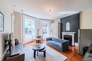 Een moderne woonkamer met een open haard, een bank, een eethoek met stoelen en een keuken met een koelkast.