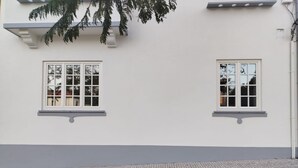 Un bâtiment avec deux fenêtres, un mur inférieur de couleur grise et un sol pavé de pierres.