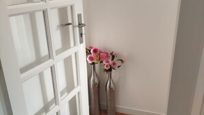 Une porte blanche ornée d’un motif quadrillé, deux vases métalliques contenant des fleurs et un plancher en bois.