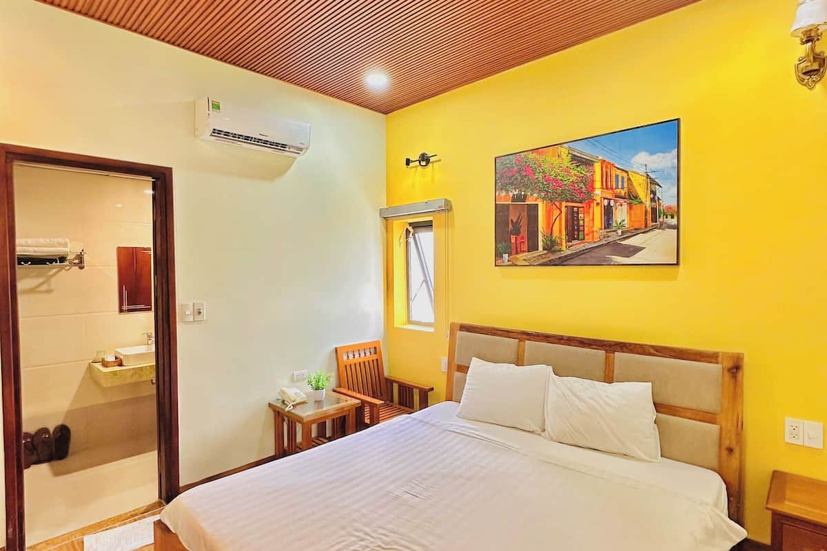 A hotel room with a wooden ceiling, a bed with white linens, a painting on the wall, and a window.