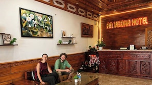 Un área de recepción con un mostrador de madera, un cuadro grande de flores y un letrero de neón que dice 'AN VELORA HOTEL'.