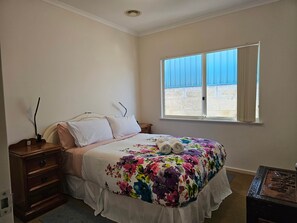 Camera da letto con un letto, un comodino, una cassettiera, una finestra con persiane e vista sull'esterno.