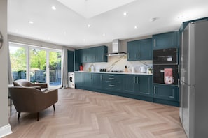 A modern kitchen with teal cabinets, a stainless steel refrigerator, and a herringbone wood floor. - Stylish 5 Bed Surrey Home with Garden (Leatherhead)