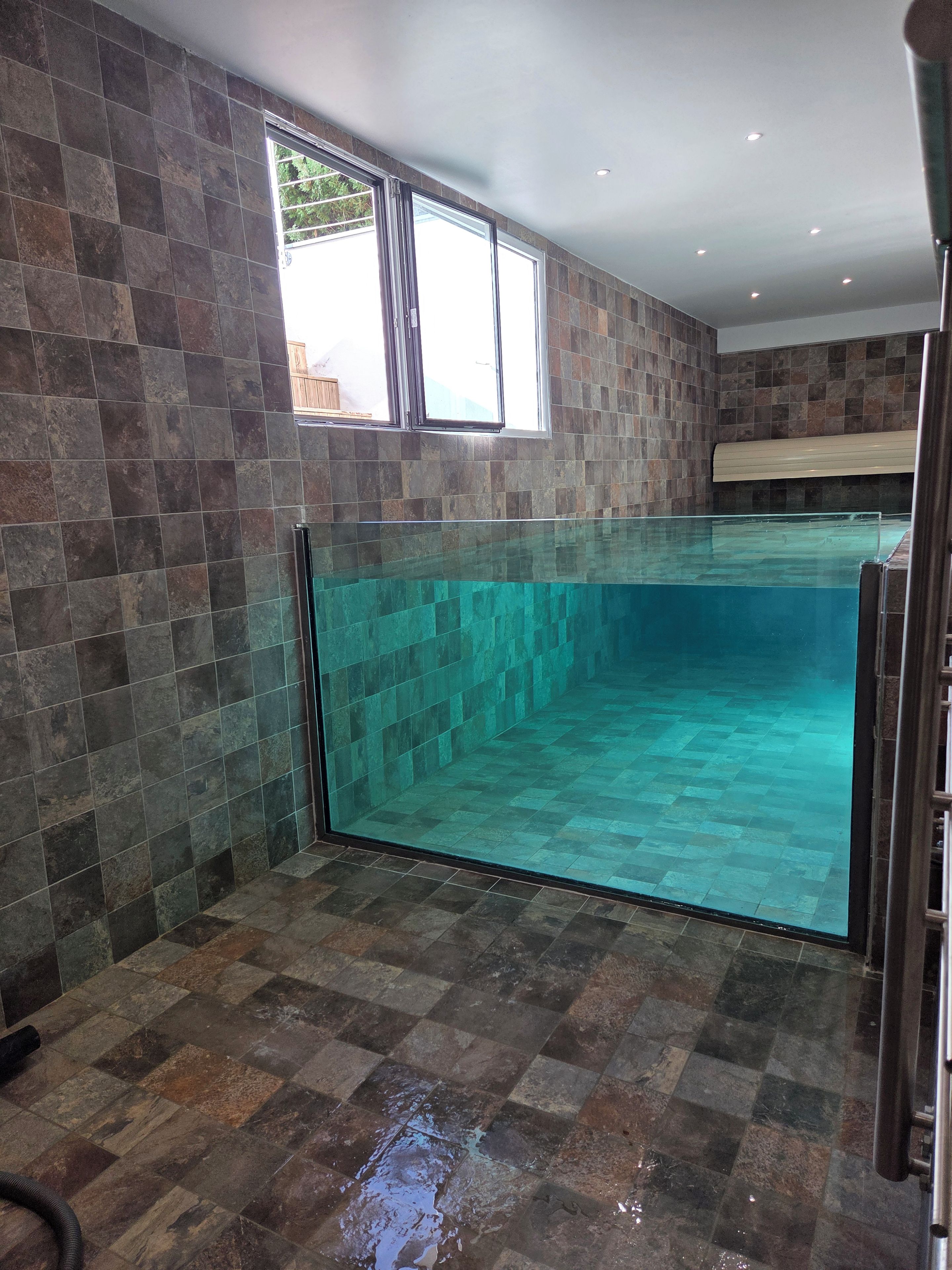 A swimming pool with clear water, surrounded by stone tiles, and a window above it.