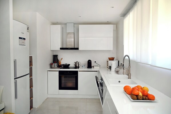 A modern kitchen with white cabinetry, a built-in oven, and a fruit bowl on the counter.