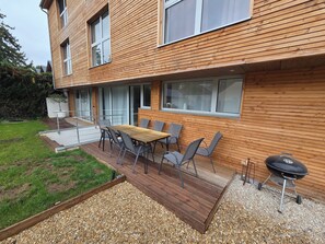 Una casa moderna con terraza, mobiliario exterior y una parrilla.