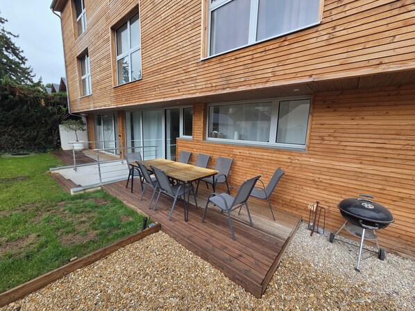 Una casa moderna con terraza, mobiliario exterior y una parrilla.
