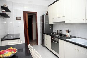A kitchen with white cabinets, a black countertop, a refrigerator, a stove, and a sink. - VicoStay by Casa Stella: Relaxation with a View in the Heart of the Sorrento Coast (Vico Equense)