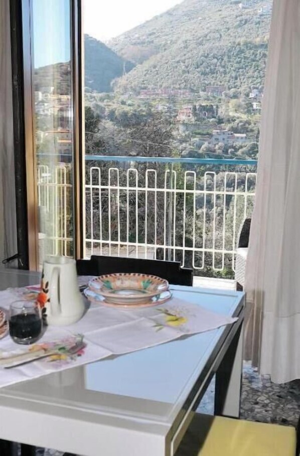 A balcony with a metal railing, a table with a white tablecloth, and a view of a mountainous landscape. - VicoStay by Casa Stella: Relaxation with a View in the Heart of the Sorrento Coast (Vico Equense)