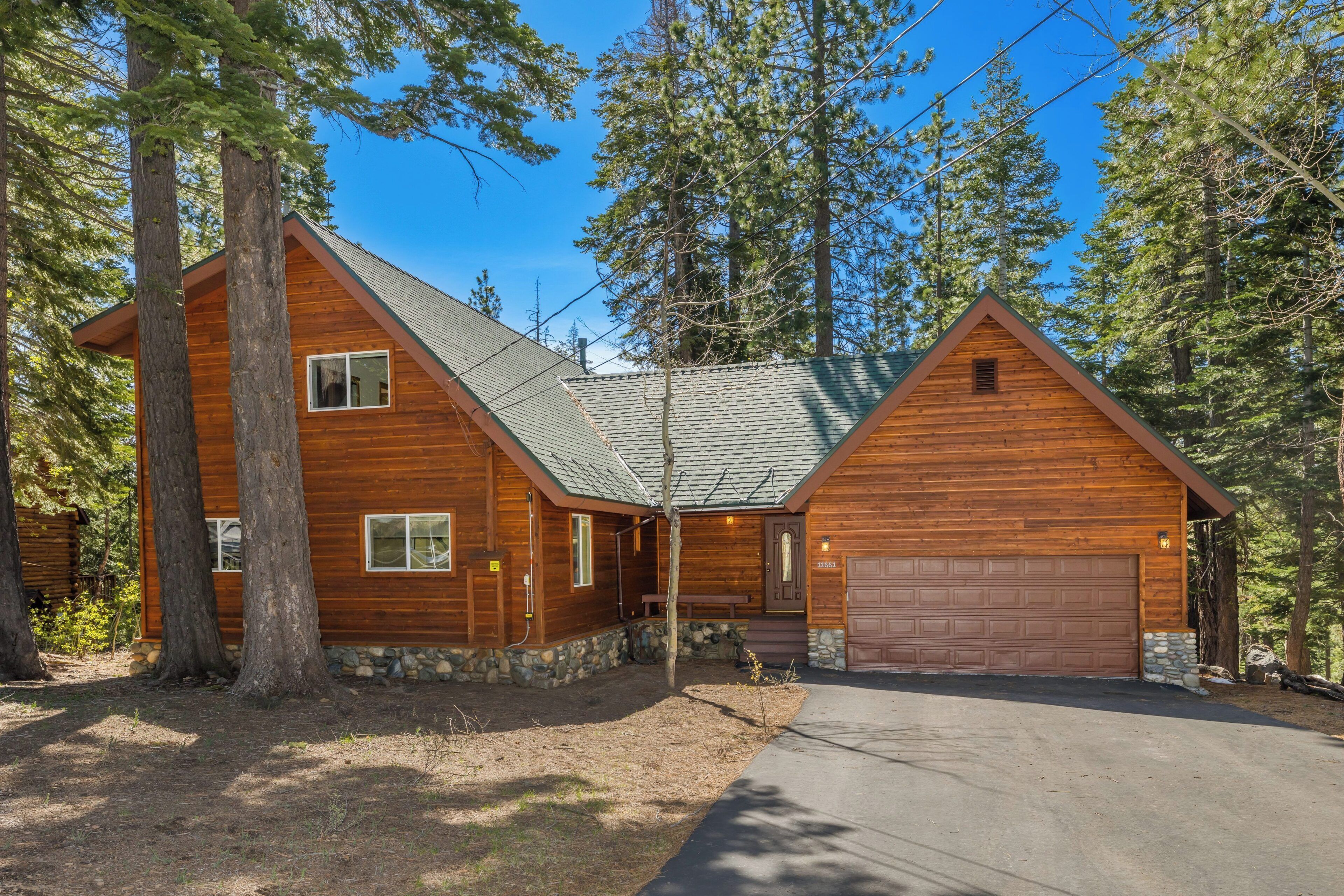 A wooden cabin with a stone foundation, a garage, and a covered porch.