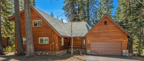 A wooden cabin with a stone foundation, a garage, and a covered porch.