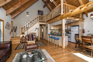 A spacious living area with a wooden staircase, a kitchen with bar stools, and a dining table with chairs. - Timberline Lodge_AC, Sauna, Shuffleboard (Truckee)