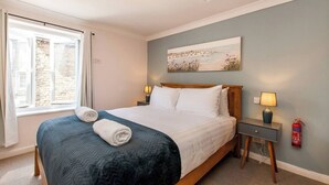 Habitación de hotel con cama, dos lámparas de noche, un cuadro en la pared y una ventana con cortinas.