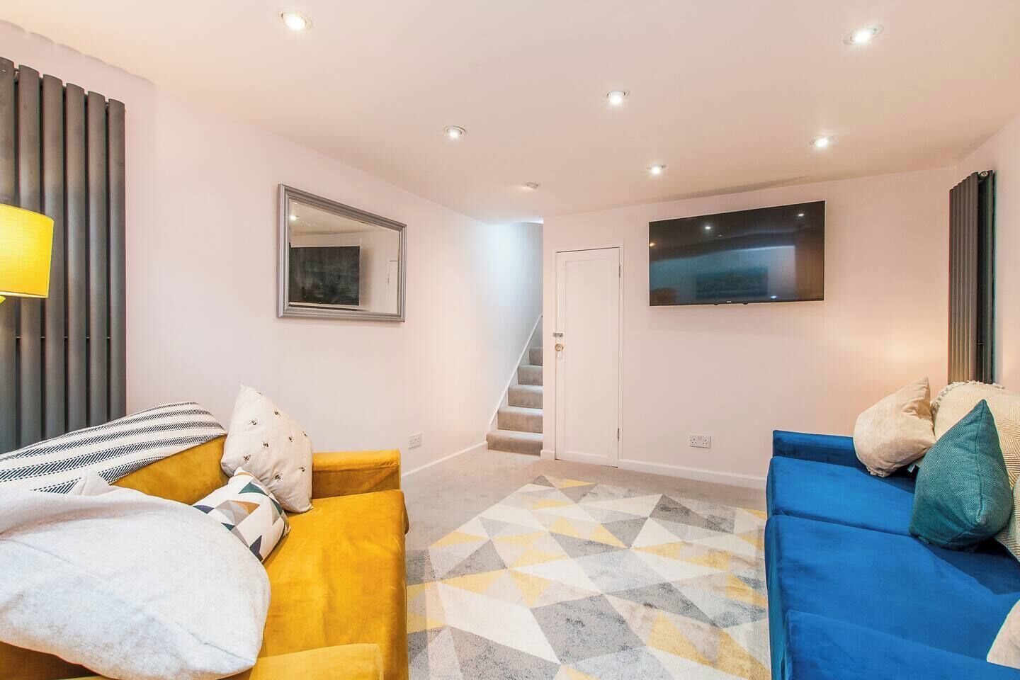 Una sala de estar moderna con un sofá, un televisor montado en la pared y una escalera que lleva a otra habitación.