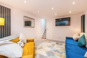 A modern living room with a sofa, a TV mounted on the wall, and a staircase leading to another room. - The Salty Crab Ramsgate Holiday Home (Kent)