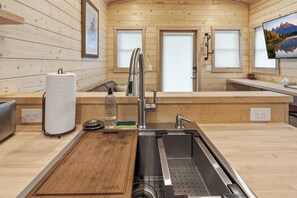 Una cocina moderna con paredes de madera, un lavamanos de acero inoxidable y una tabla de cortar de madera.